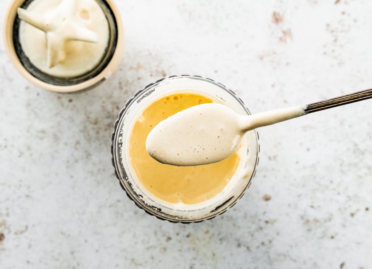 Creamy tahini sauce being scooped up by a silver spoon from the base of a blender.
