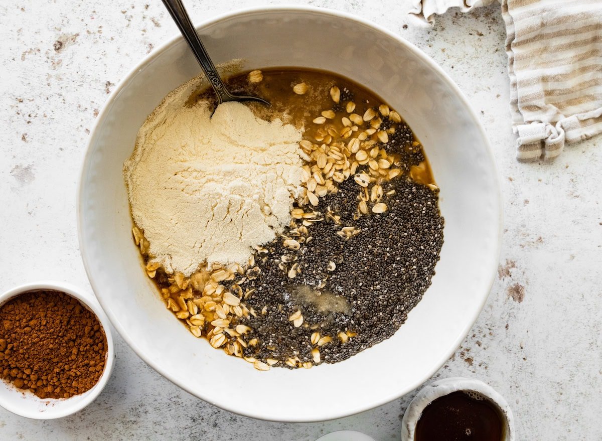 Unmixed ingredients for tiramisu overnight oats in a bowl, including oats, chia seeds, protein powder, and coffee.