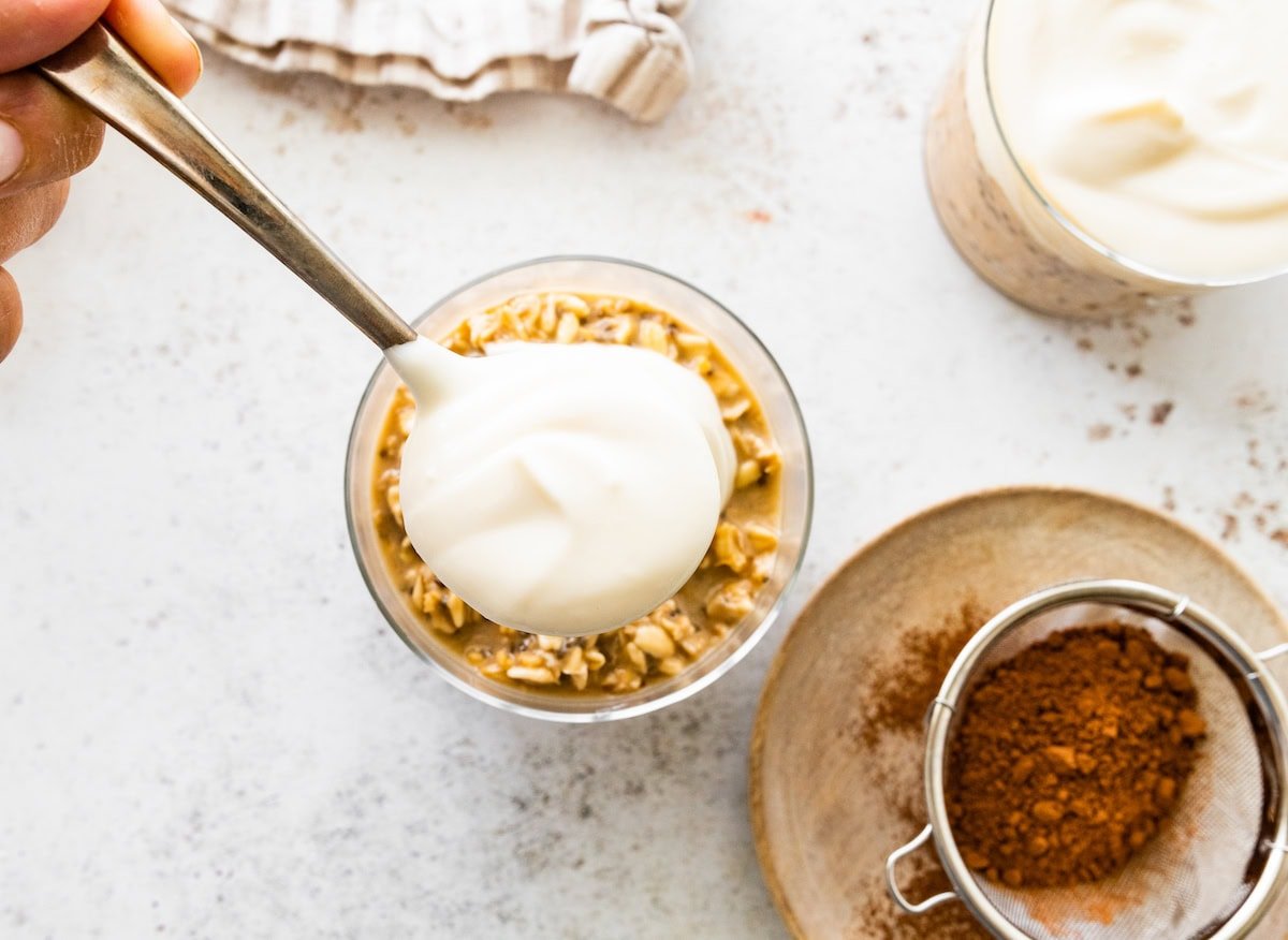 Spooning the yogurt “mascarpone” layer over the coffee oat mixture in a glass jar.