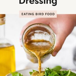 A hand pours Italian dressing from a jar onto a fresh green salad, with a bottle of oil in the background.