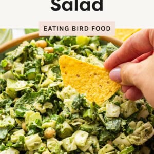 Close-up of Green Goddess Salad with chopped greens, chickpeas, and creamy dressing, as a hand dips a tortilla chip into the bowl.