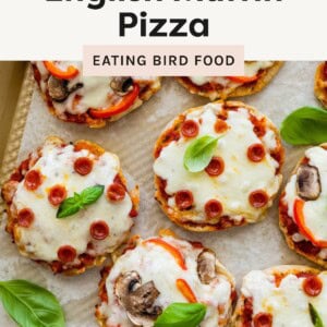 ChatGPT said: Overhead view of mini English muffin pizzas topped with melted cheese, mini pepperoni, red peppers, mushrooms, and basil leaves on a baking sheet.