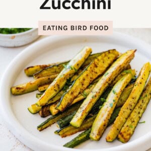 Plate of roasted zucchini sticks garnished with herbs on a white plate.