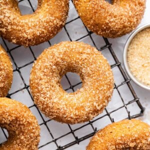Freshly baked apple cider donuts coated in cinnamon sugar cooling on a wire rack.
