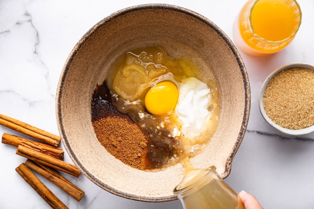 Bowl of wet ingredients including egg, applesauce, and spices being prepared for apple cider donut batter.