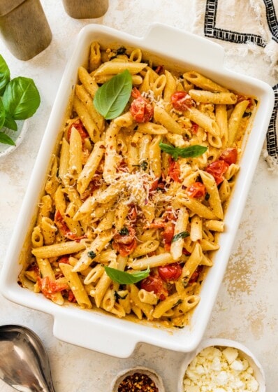 Baked feta pasta in a white baking dish topped with basil and grated parmesan.