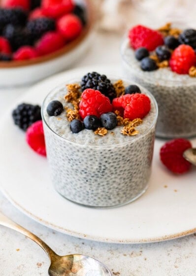 Glass of basil seed pudding topped with berries and granola on a white plate.