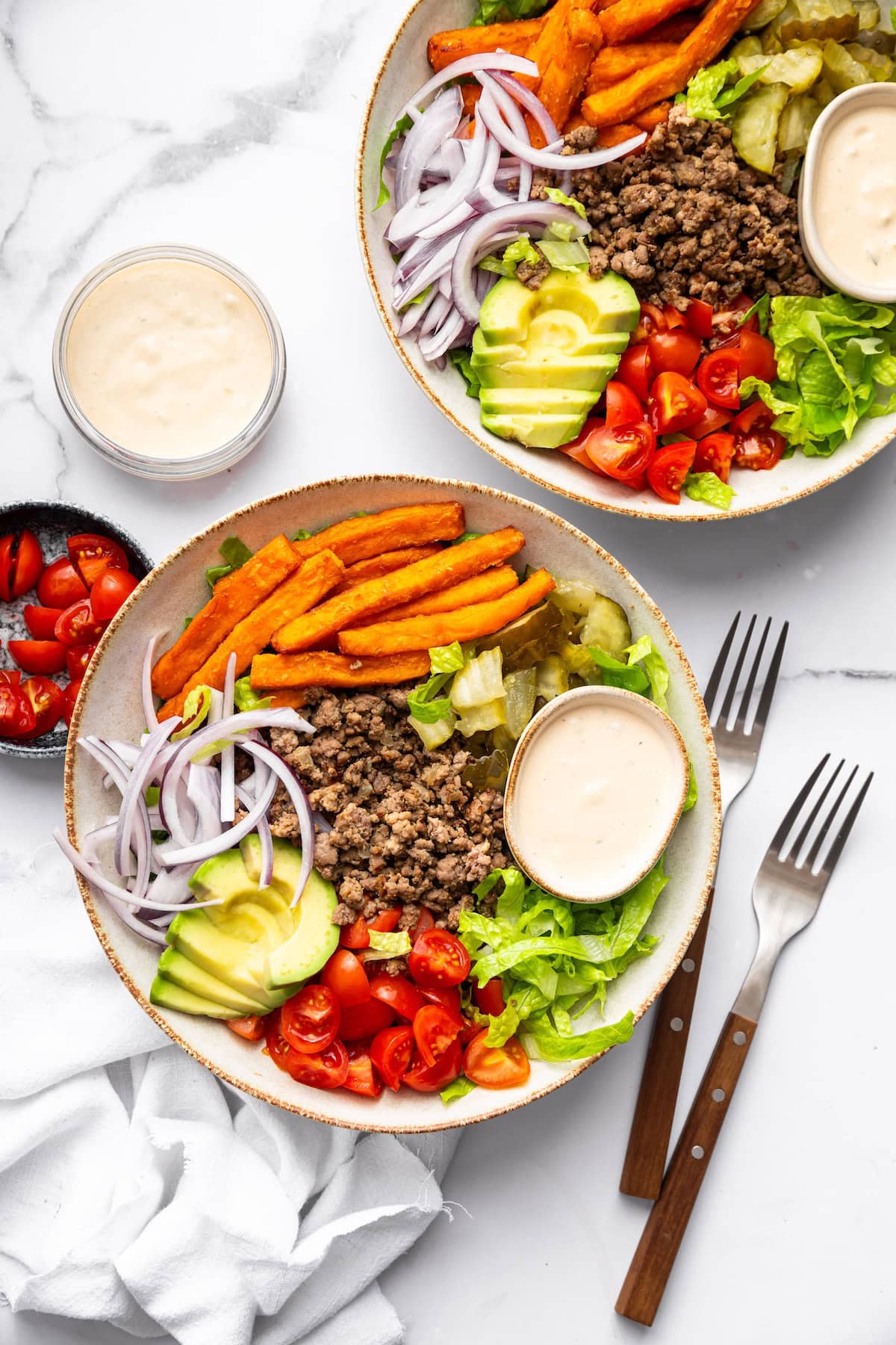 Two burger bowls with sweet potato fries and a small bowl of Big Mac sauce in the bowls.