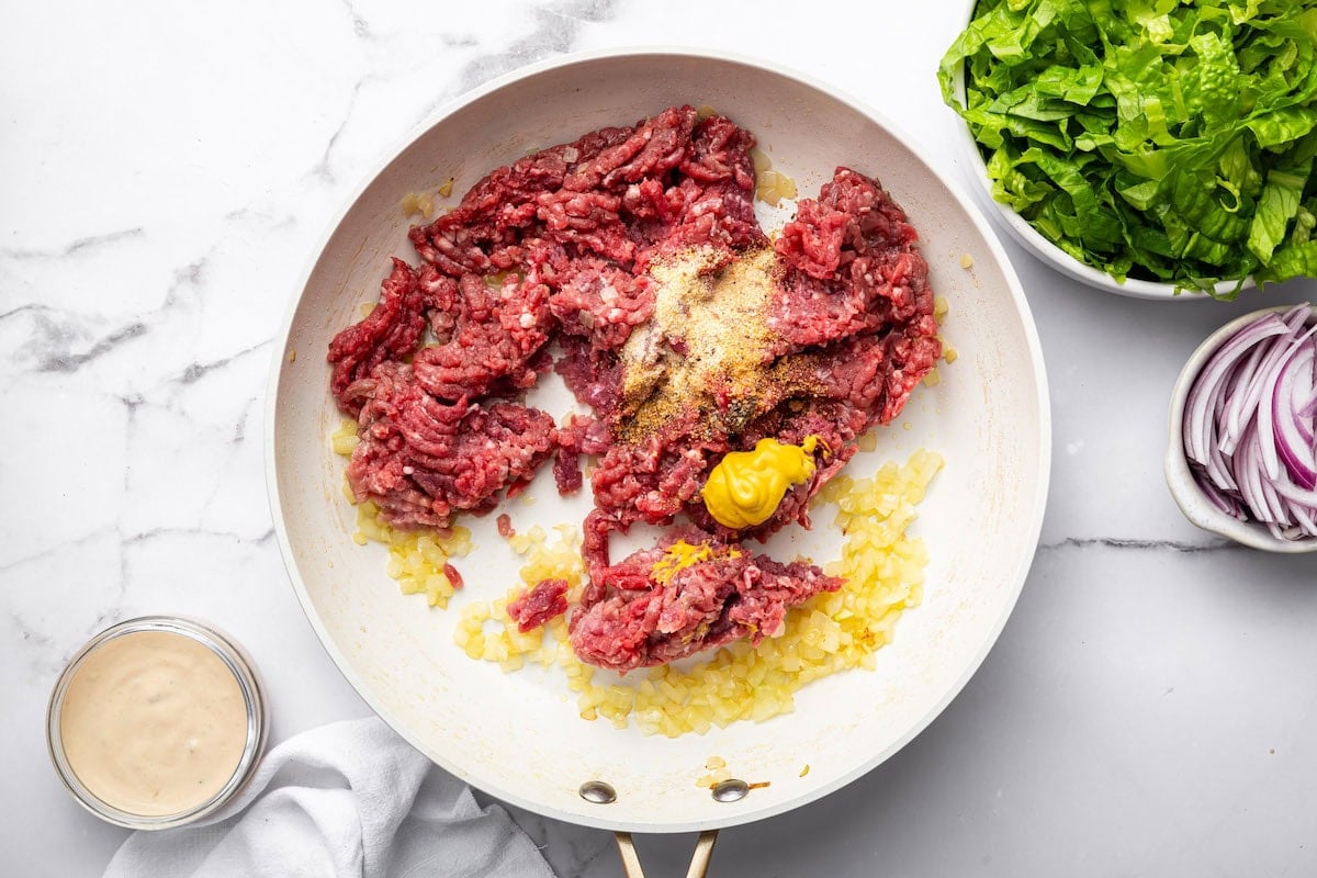 Raw ground beef in a pan with mustard and spices.