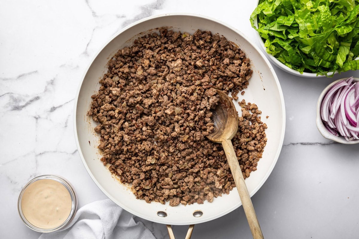 Ground beef cooked in a skillet with a wooden spoon.
