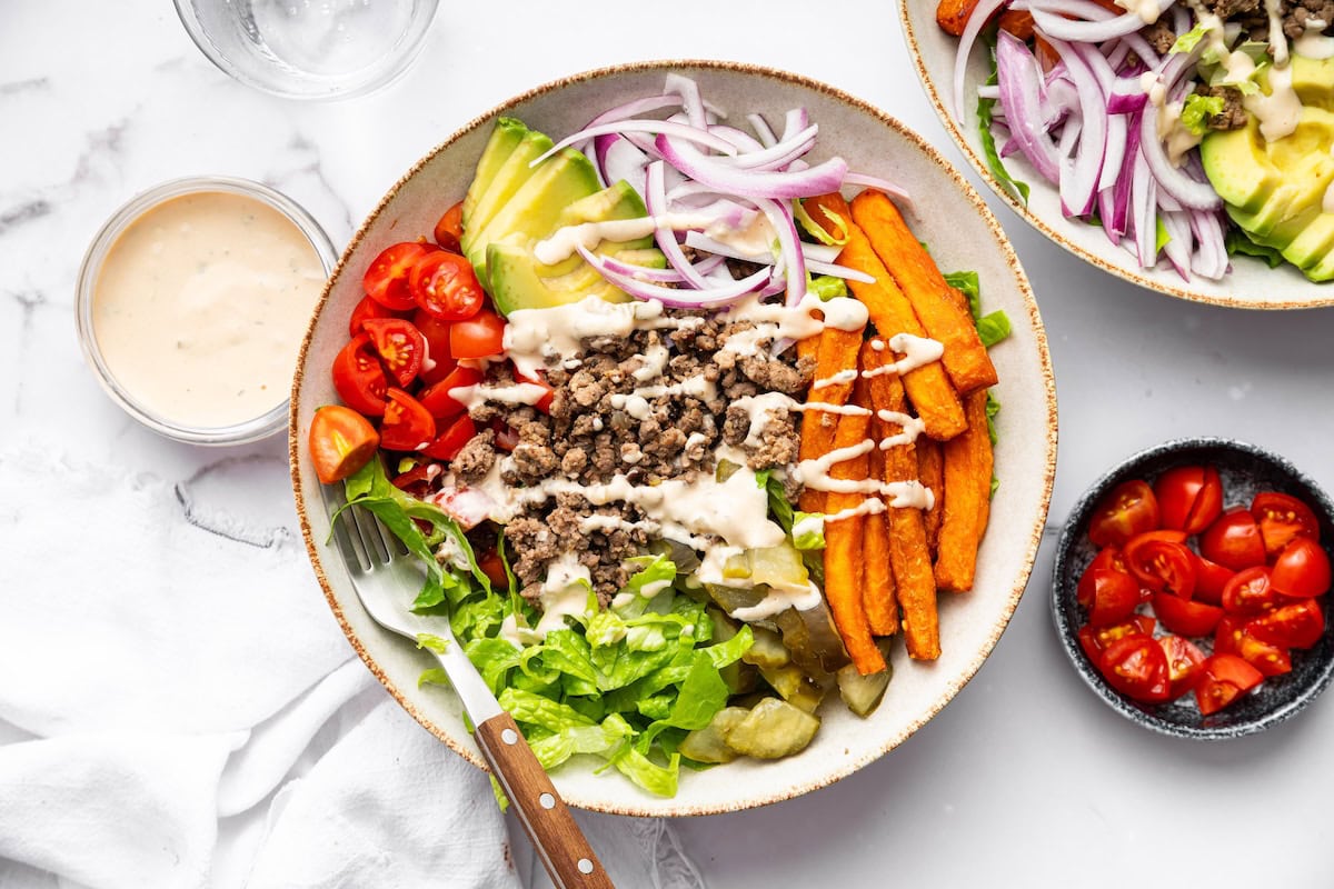 Burger bowl with ground beef, sweet potato fries, avocado, tomato, red onion, pickles, lettuce and a drizzle of Big Mac sauce.
