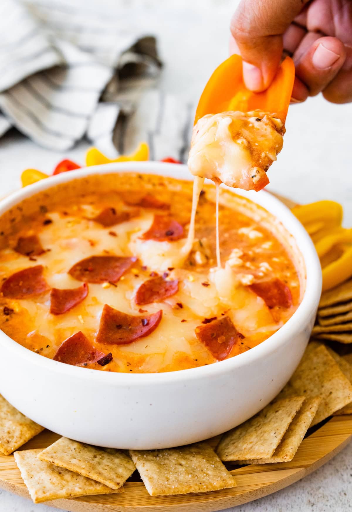 Cottage cheese pizza bowl with turkey pepperoni and melted mozzarella, with a hand dipping a cracker into the bowl showing a cheese pull.