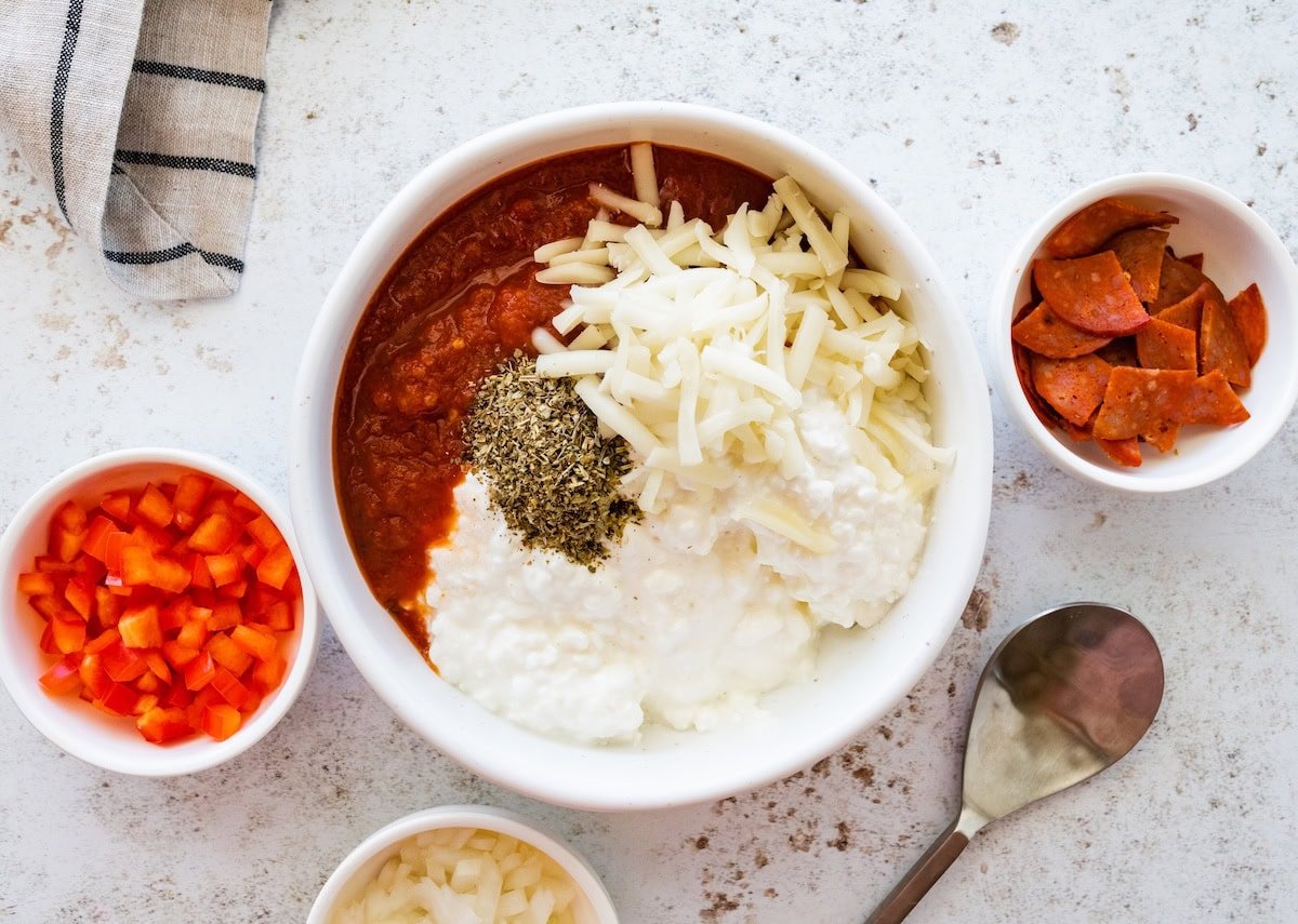 Cottage cheese, marinara sauce, shredded mozzarella and Italian seasoning in a bowl before mixing for a high protein pizza bowl.