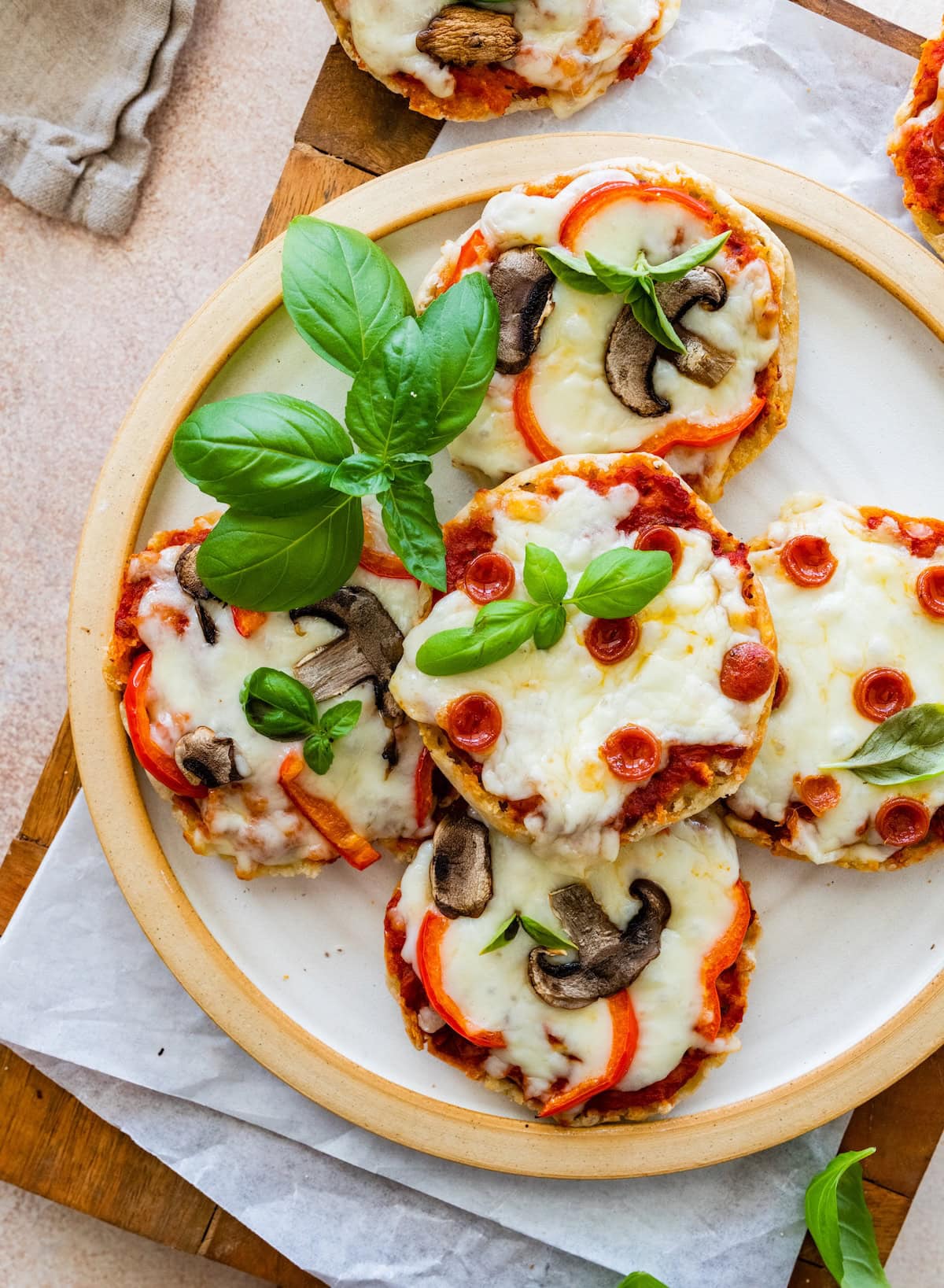 Plate of English muffin pizzas stacked and garnished with basil leaves.