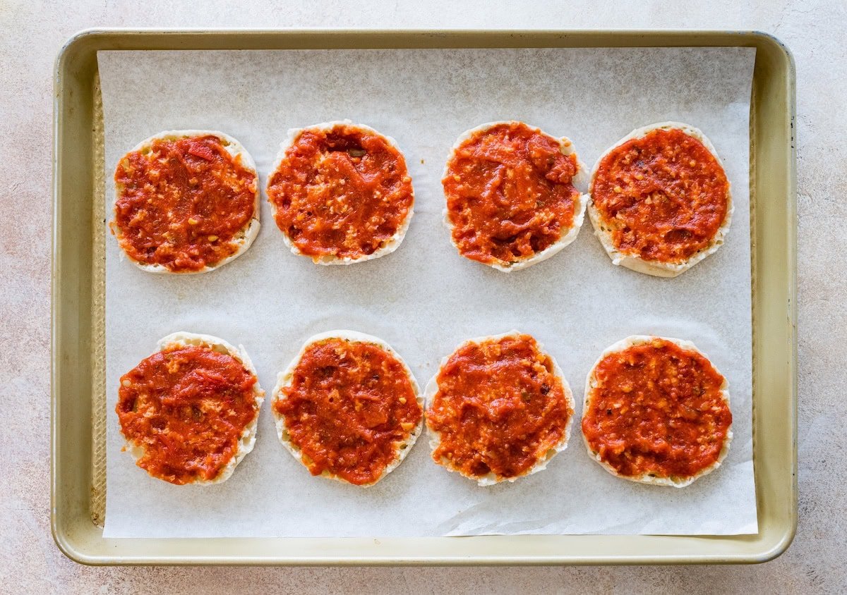 English muffin halves topped with pizza sauce, ready for cheese and toppings.