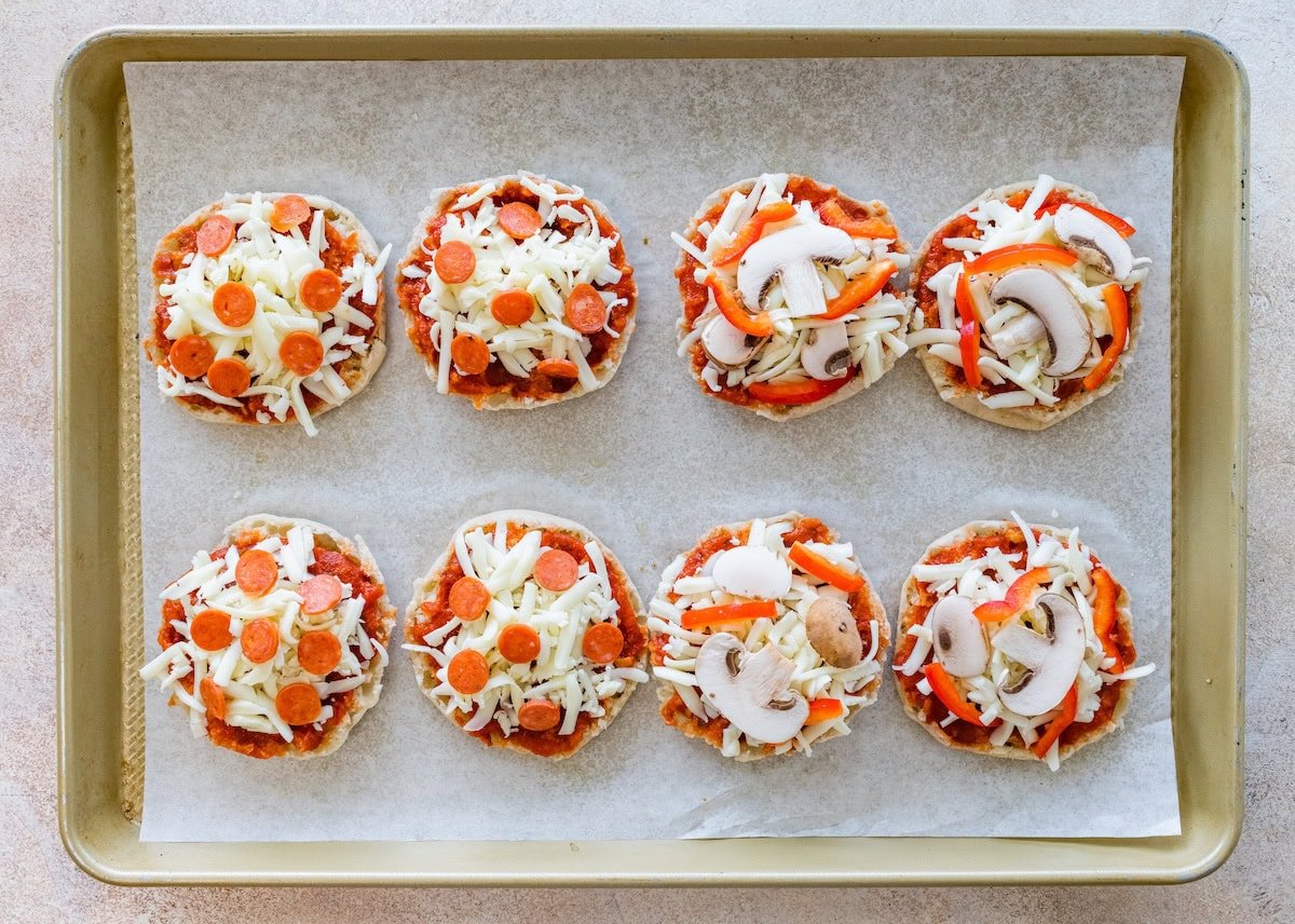 English muffins topped with sauce, cheese, and toppings before baking.
