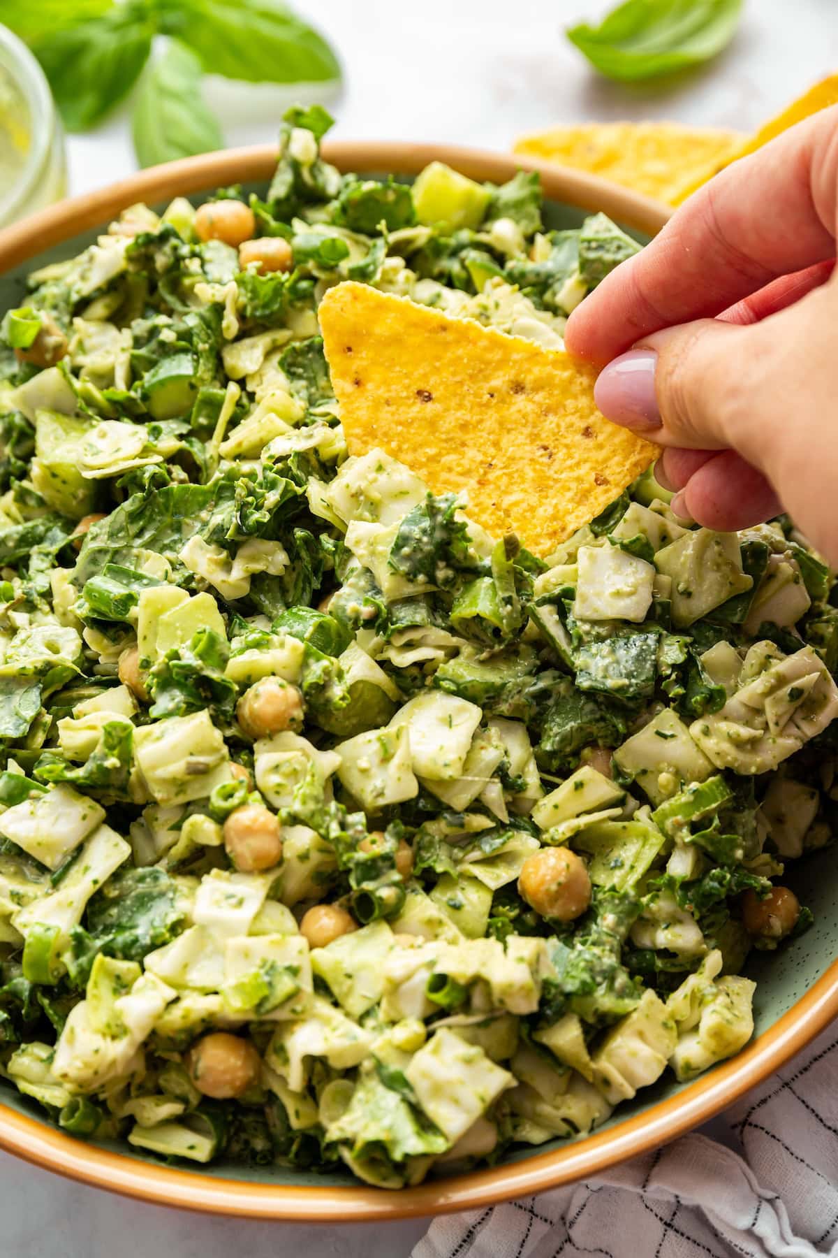 Hand dipping a tortilla chip into creamy green goddess salad, showcasing the dip-friendly texture.