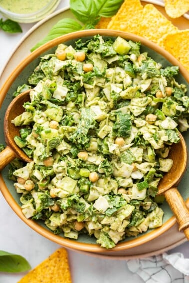 Green goddess salad with wooden salad servers, served with tortilla chips.