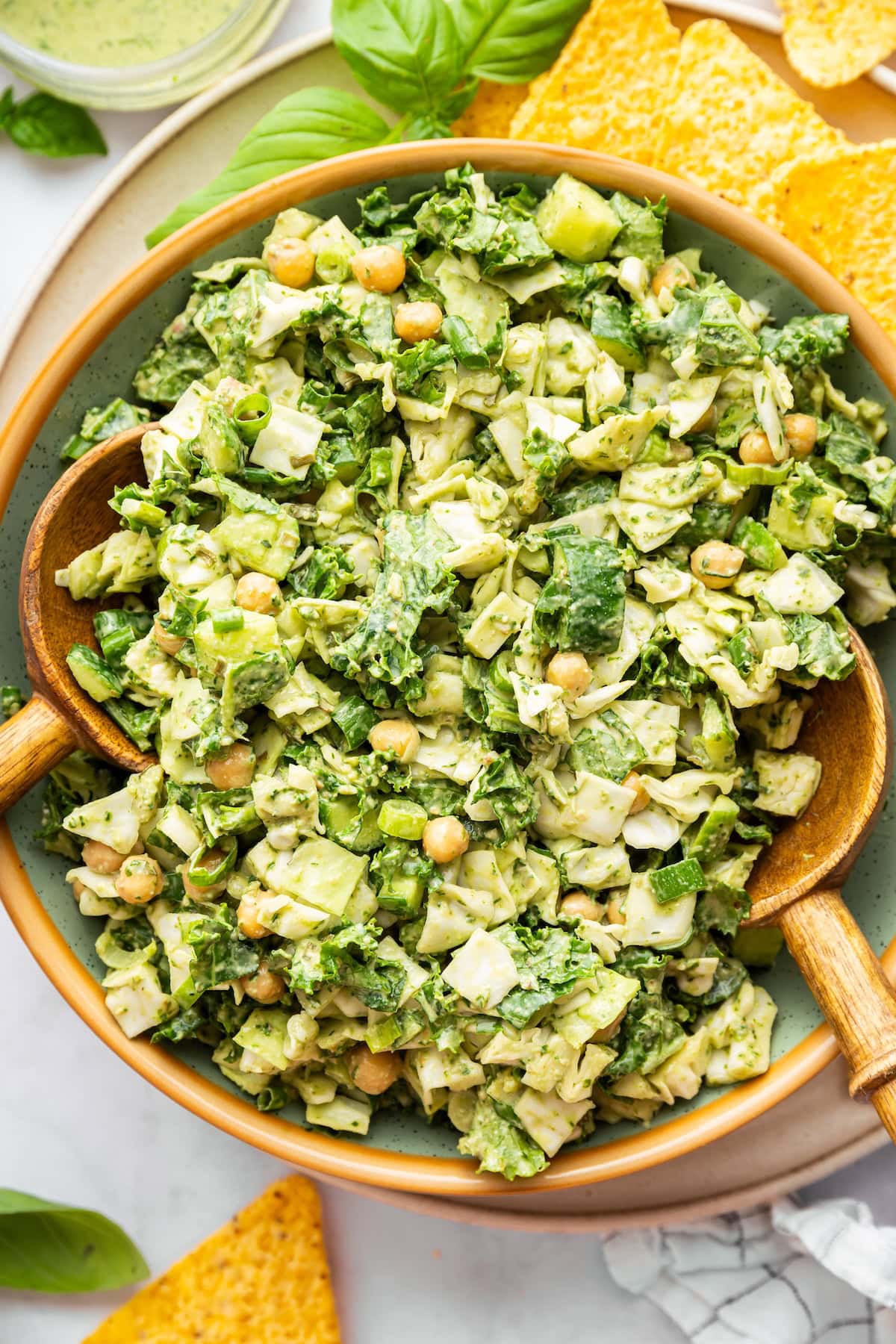 Green goddess salad with wooden salad servers, served with tortilla chips.