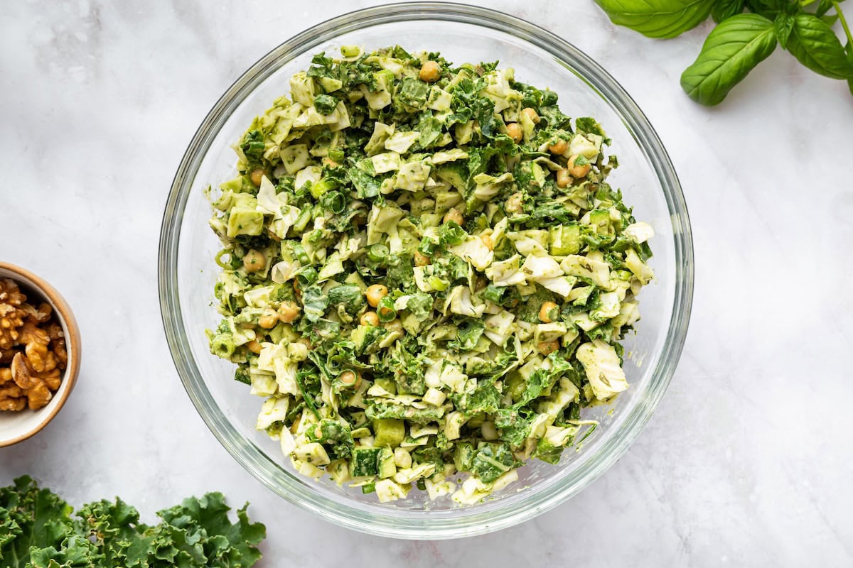 Mixed green goddess salad in a clear glass bowl with creamy herb dressing coating chopped vegetables.