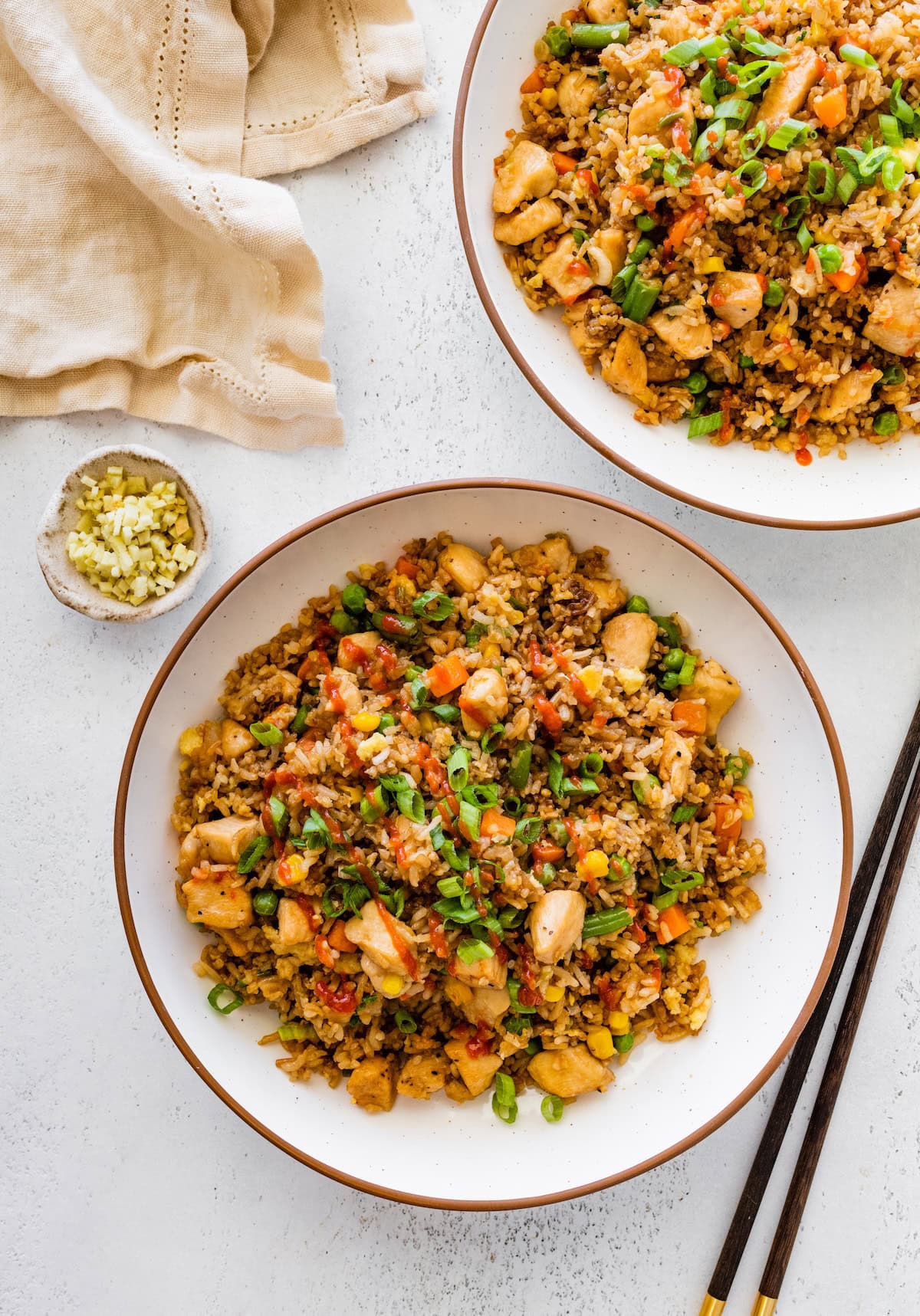 Two bowls of chicken fried rice on a white surface with chopped green onions on top.
