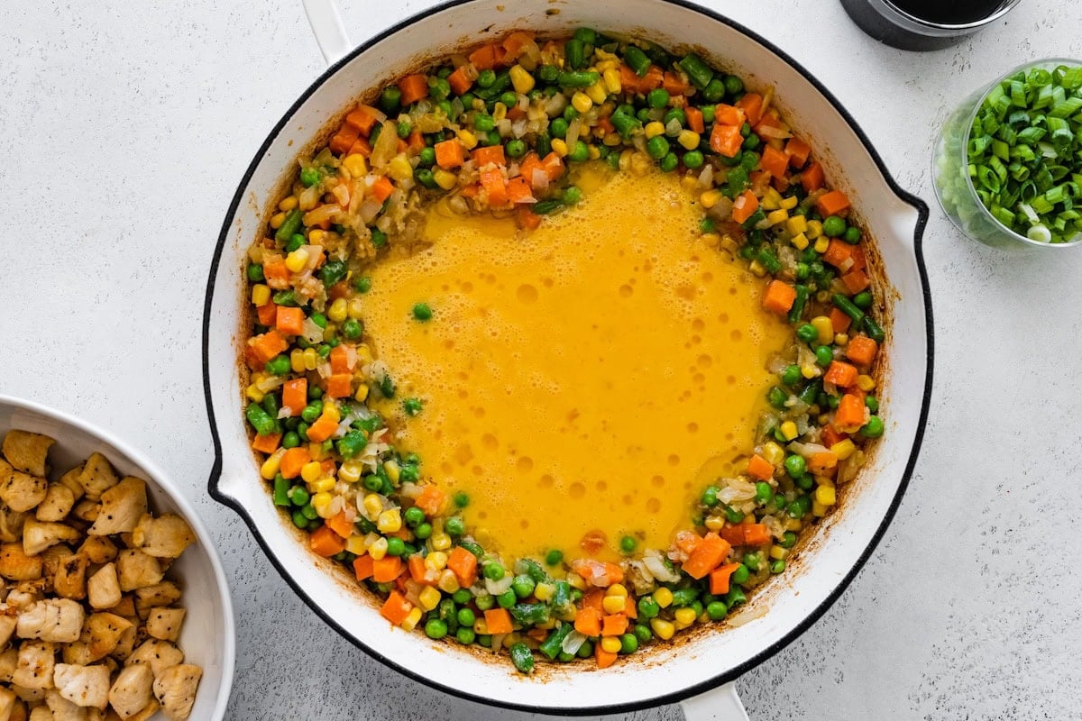 Frozen mixed vegetables cooking in a skillet with scrambled eggs in the center.