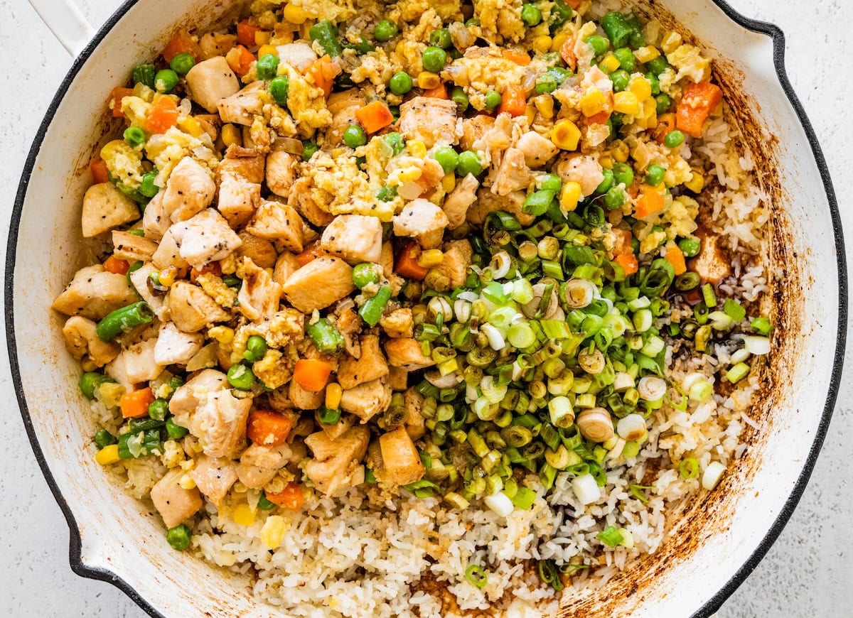 Cooked chicken, rice, and mixed vegetables combined in a skillet with chopped green onions on top.
