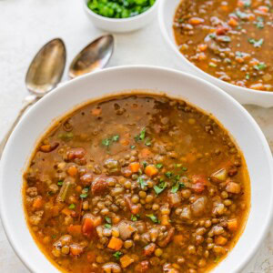 A white bowl of lentil soup with roasted garlic and vegetables.