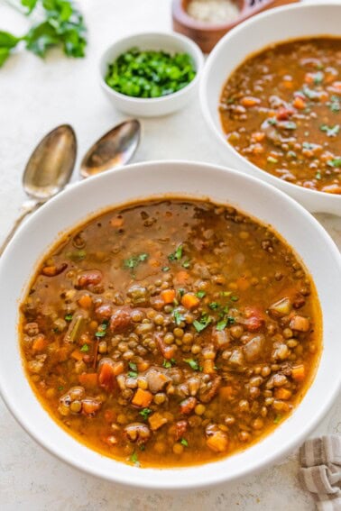 A white bowl of lentil soup with roasted garlic and vegetables.