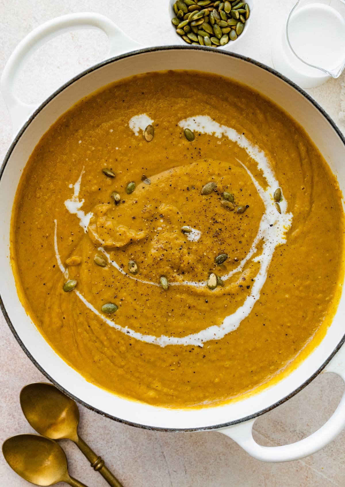 Pumpkin curry soup in a large pot with a swirl of coconut milk and pumpkin seeds on top.