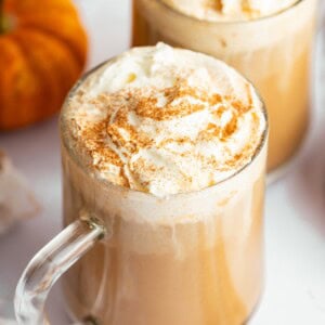 Homemade pumpkin spice latte in a glass mug topped with whipped cream and a sprinkle of cinnamon.