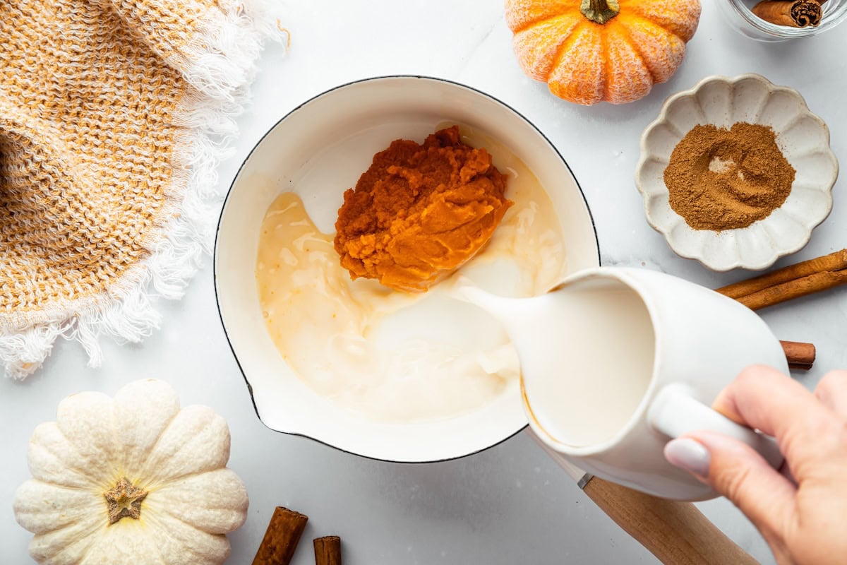 Pumpkin purée and milk being poured into a saucepan.