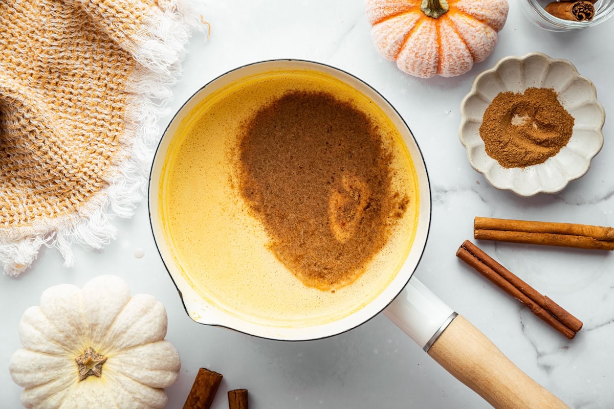 Pumpkin spice latte mixture simmering in a saucepan with cinnamon sprinkled on top.