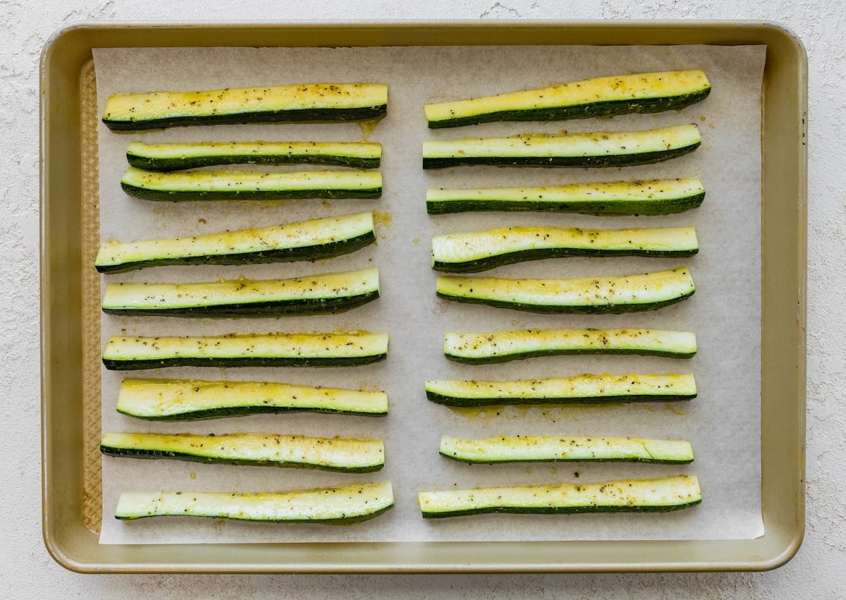 Raw zucchini sticks lined up neatly on a baking sheet before roasting.