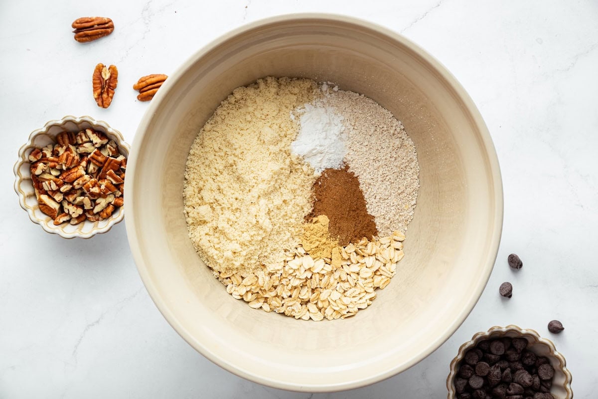 A large mixing bowl of almond flour, oat flour, cinnamon, baking powder, ground ginger, and rolled oats.
