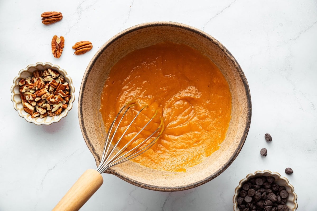 A mixing bowl of mashed sweet potato with a whisk.