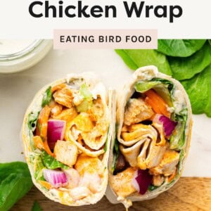 Two halves of a buffalo chicken wrap filled with chicken, lettuce, carrots, and red onion on a wooden surface.