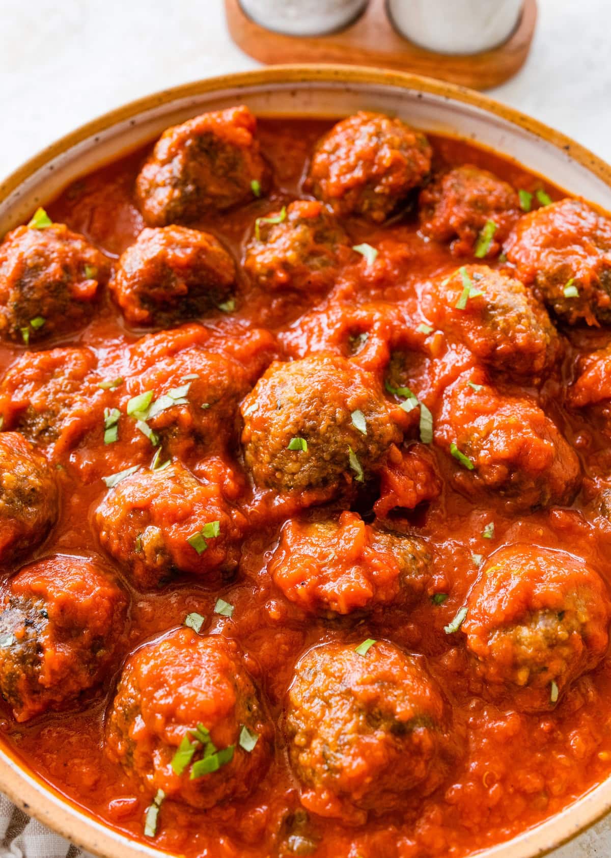 A white skillet filled with baked meatballs coated in tomato sauce.