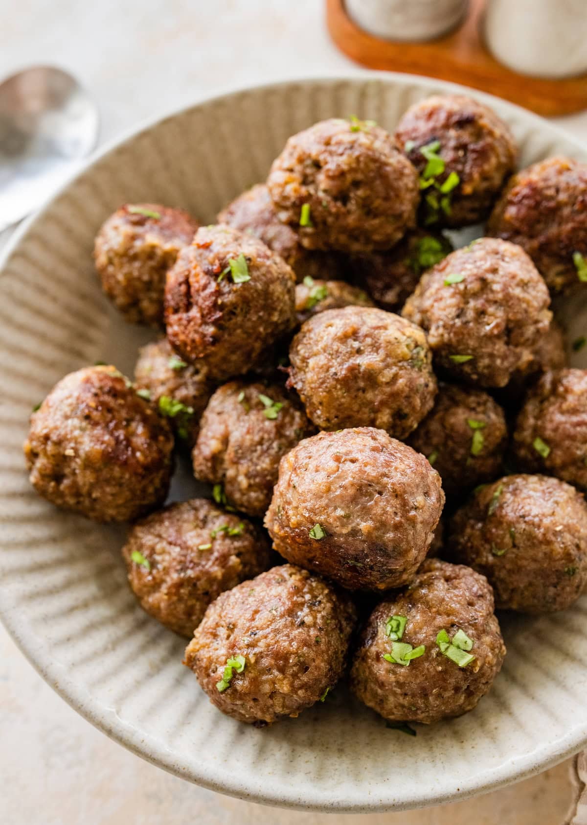 A serving bowl piled with baked beef meatballs, no sauce, garnished with herbs.