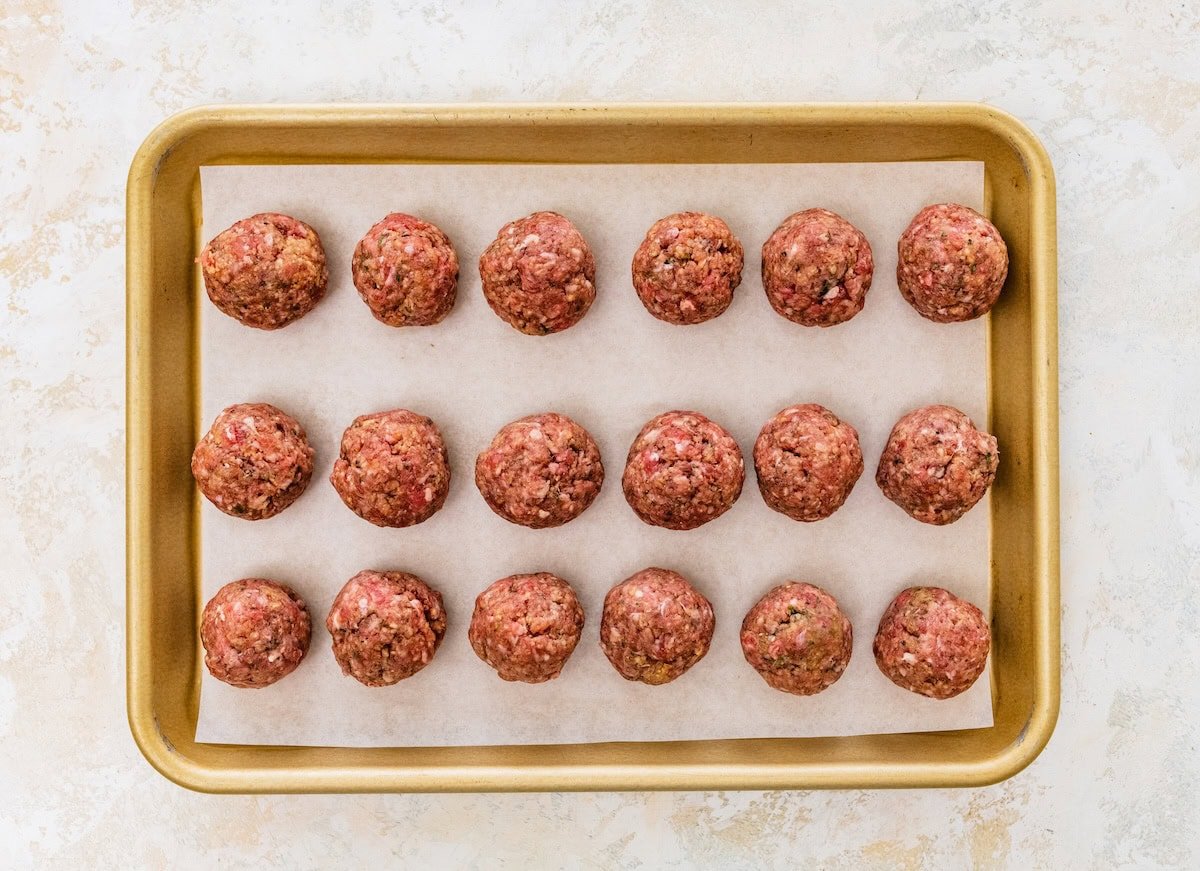Raw meatballs arranged evenly on a parchment-lined baking sheet.
