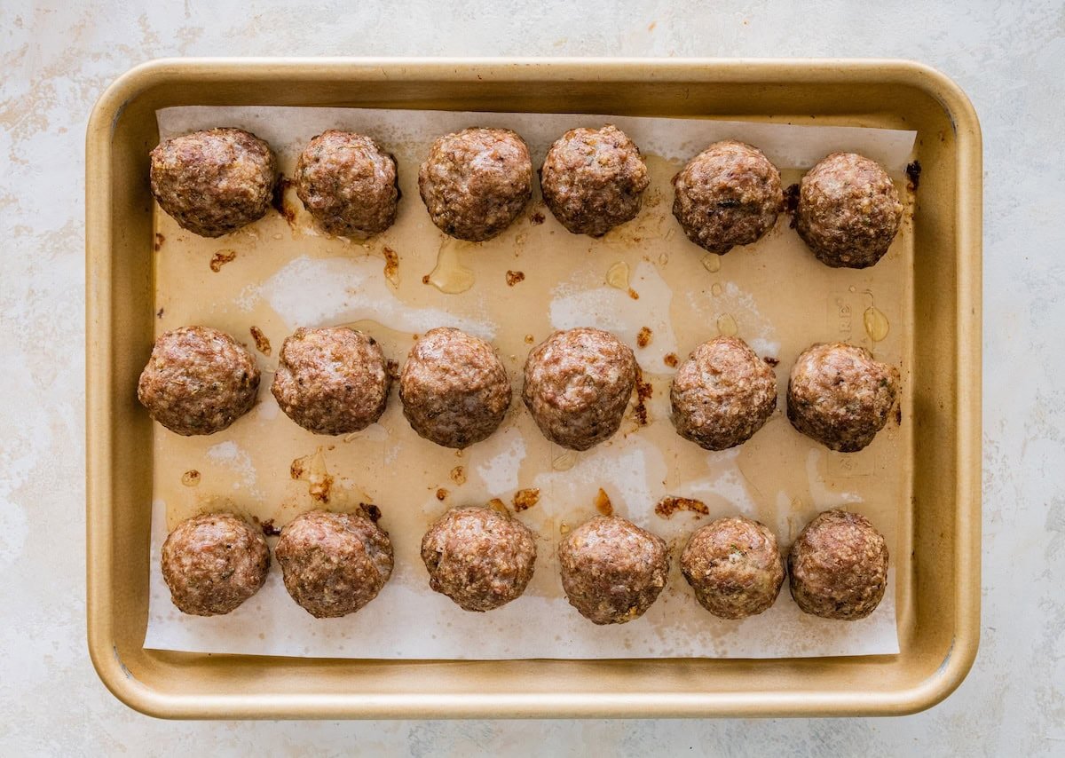 Golden brown baked meatballs fresh from the oven on a sheet pan.