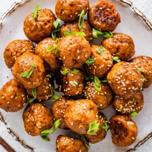 BBQ chicken meatballs on a plate topped with sesame seeds and sliced green onions.
