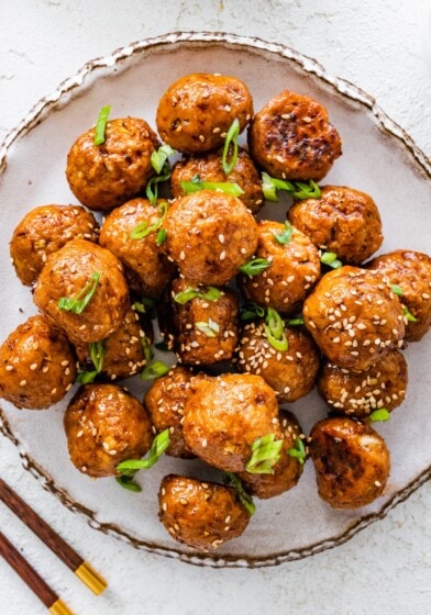 BBQ chicken meatballs on a plate topped with sesame seeds and sliced green onions.