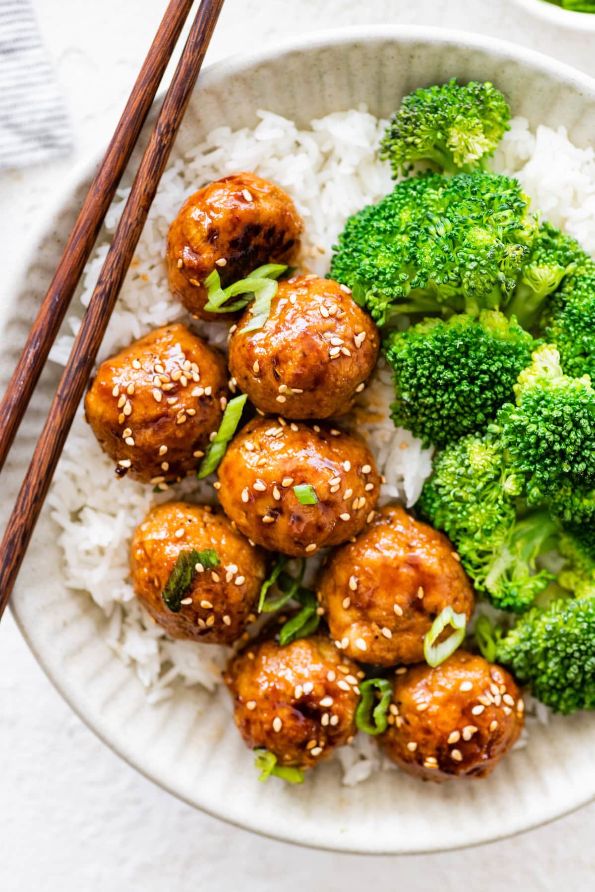 BBQ chicken meatballs served over white rice with steamed broccoli and chopsticks.