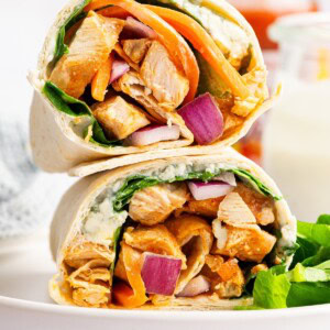 Buffalo chicken wrap halves stacked on top of each other with chicken, carrots, and onion inside.
