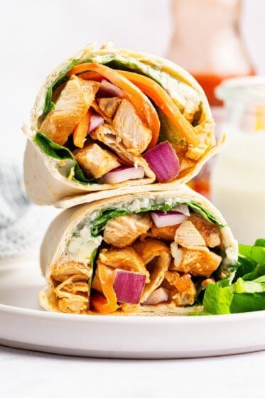 Buffalo chicken wrap halves stacked on top of each other with chicken, carrots, and onion inside.