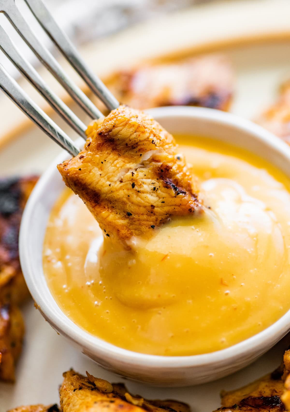 Fork dipping a grilled chicken nugget into a sauce.