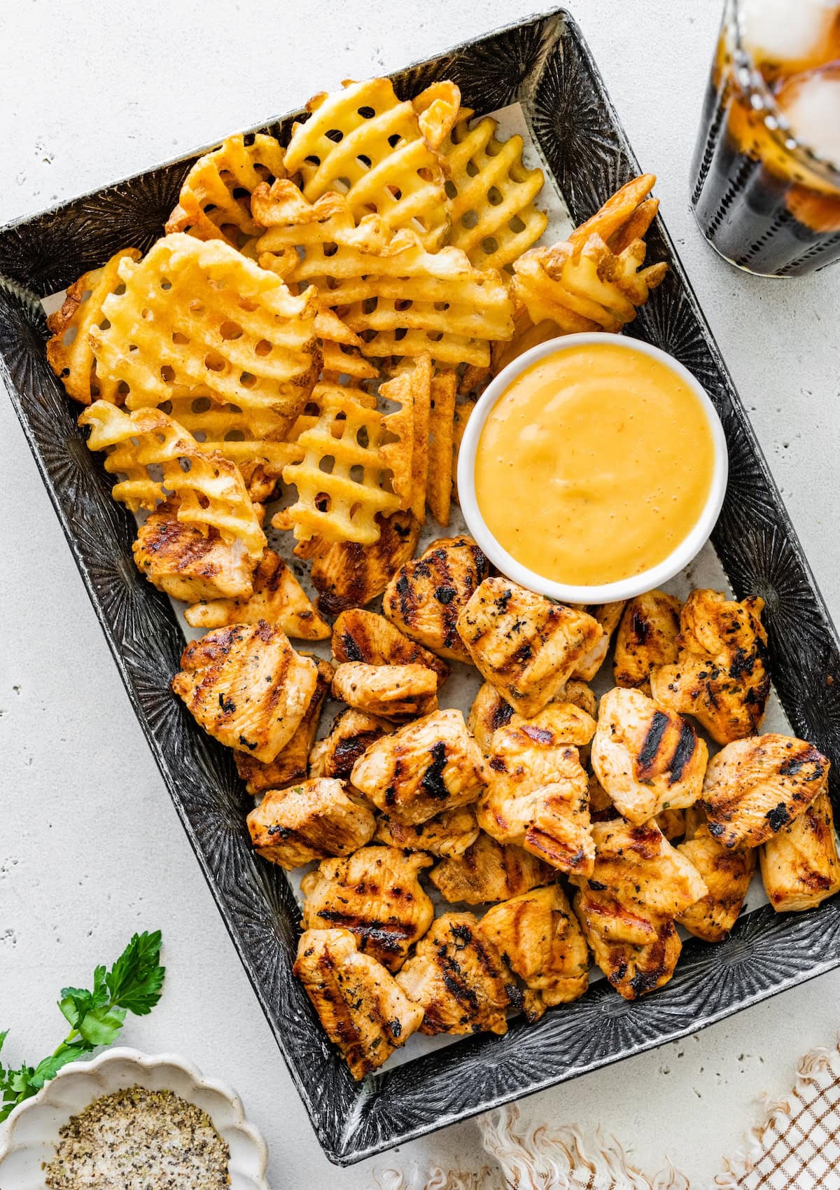 Tray of grilled chicken nuggets with waffle fries and a bowl of dipping sauce.