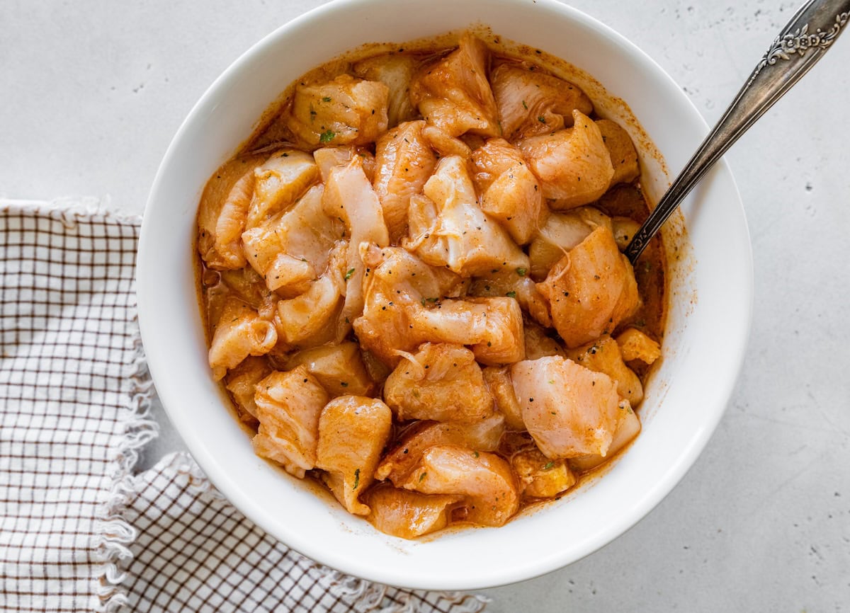 Bowl of raw chicken pieces marinated with spices and sauce, ready for grilling.