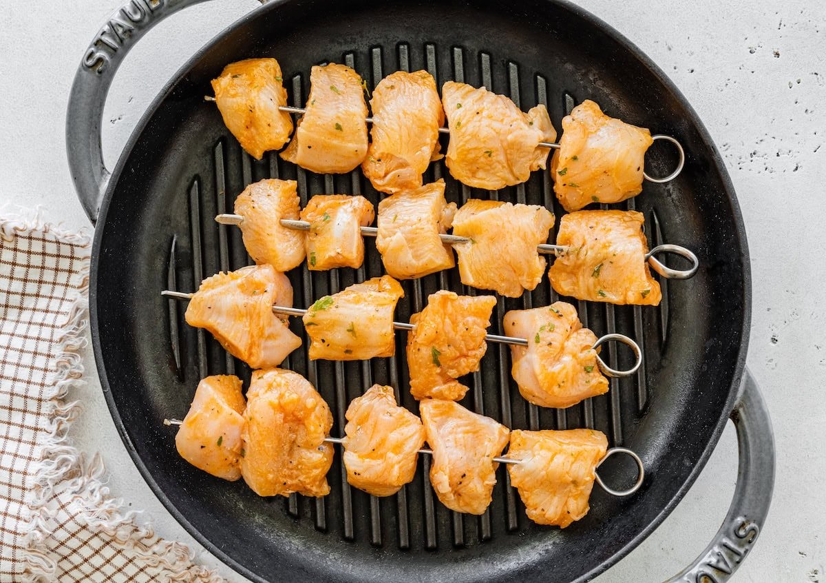 Skewers of marinated chicken arranged on a grill pan before cooking.